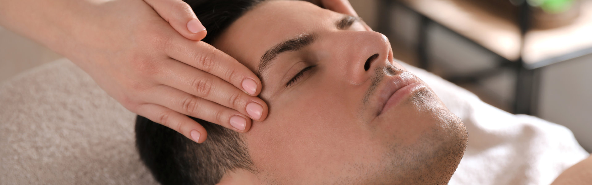 Person receiving a head massage in a spa setting, lying on a towel-covered surface with hands gently massaging their scalp.