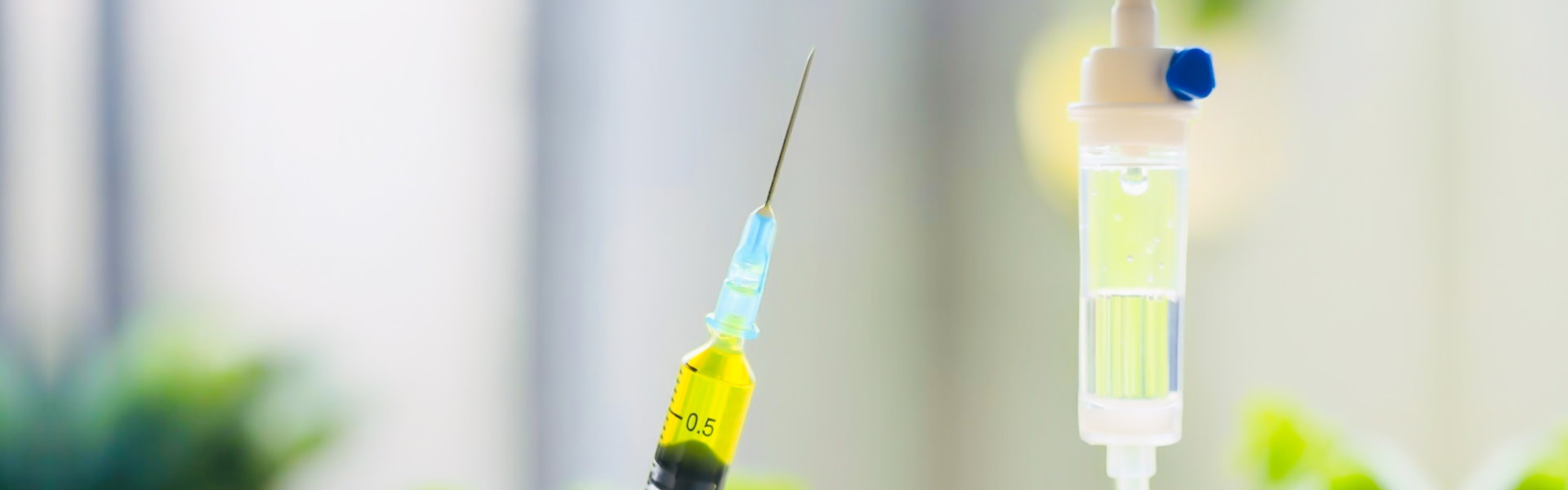 A gloved hand holds a syringe filled with yellow liquid, positioned near an IV drip. Blurred vegetables are visible in the background.